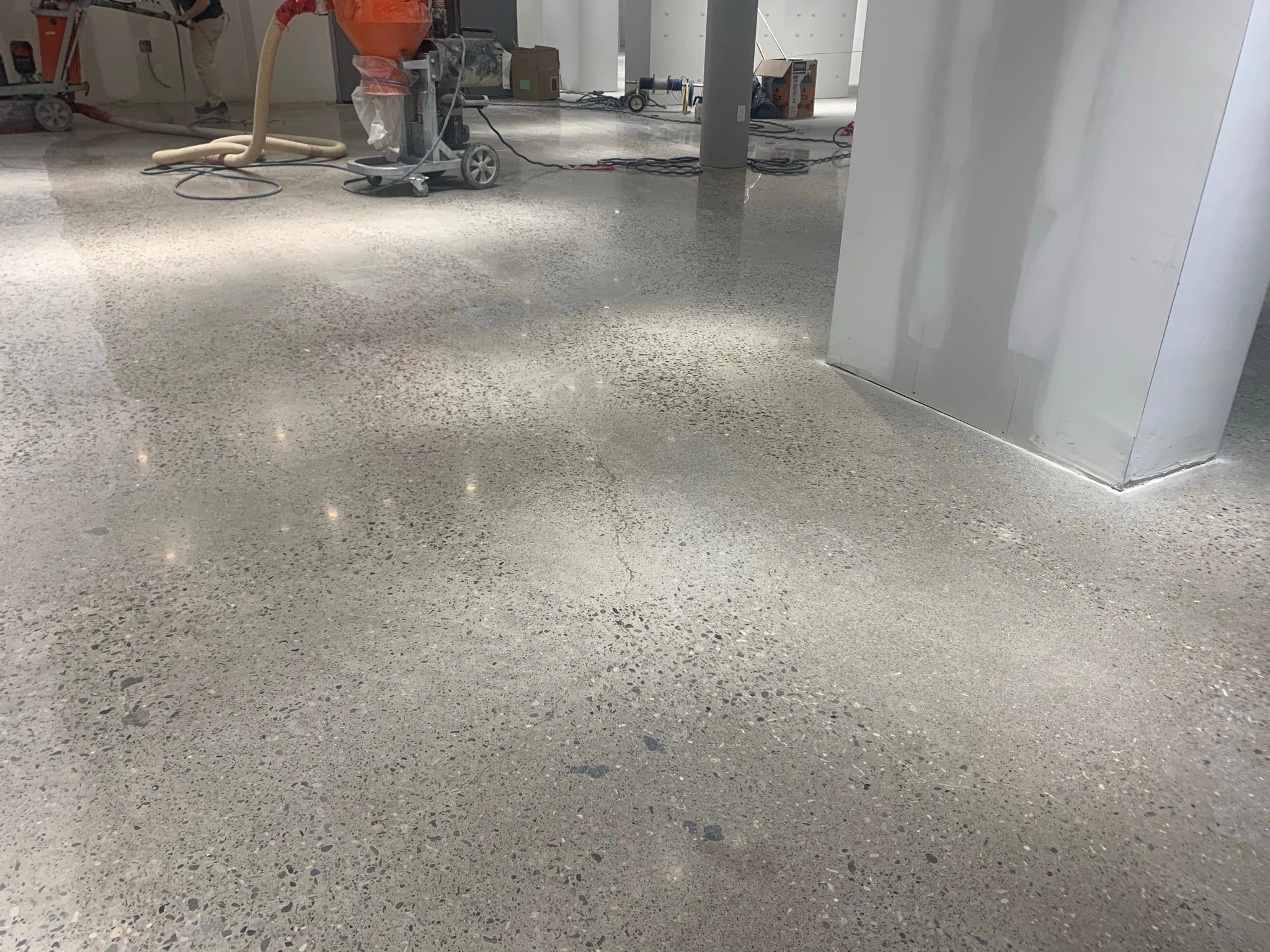 Freshly polished concrete reflecting the ceiling lights, with a polishing machine and dust extractor at work behind